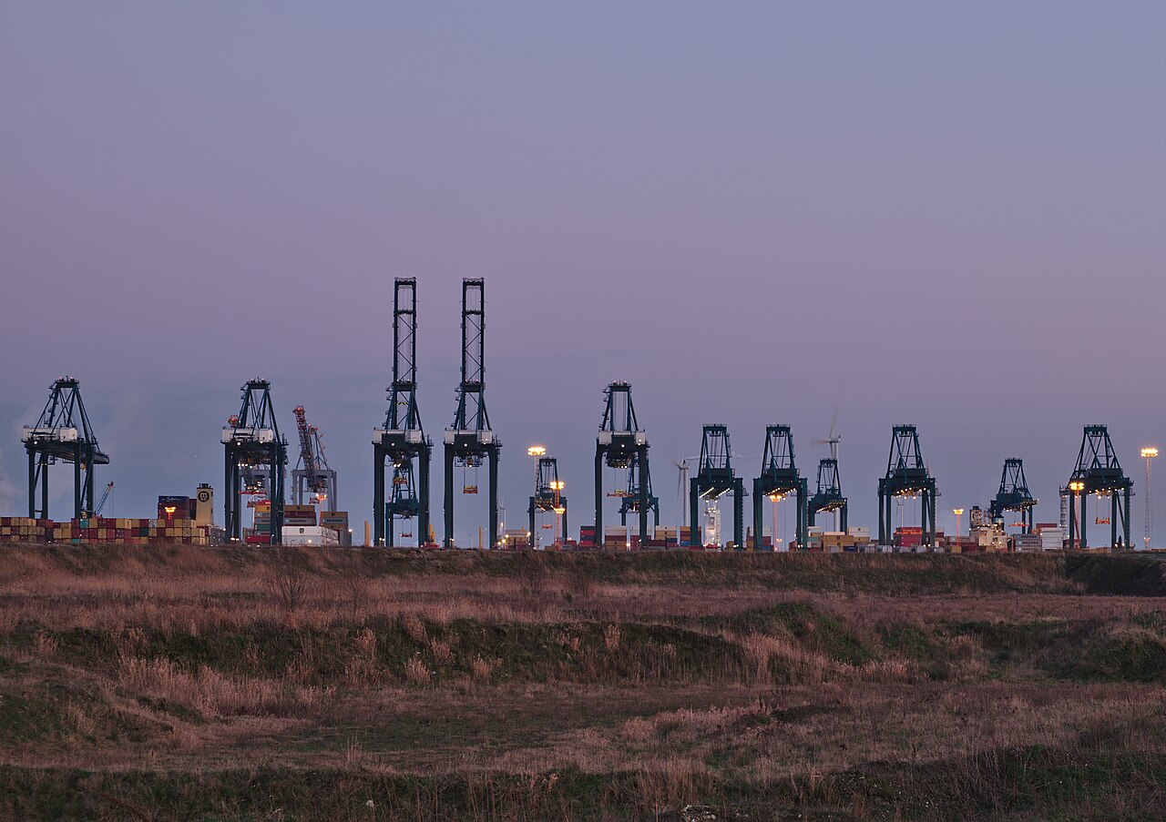 A row of container cranes silhouetted against a dusk sky at a port terminal